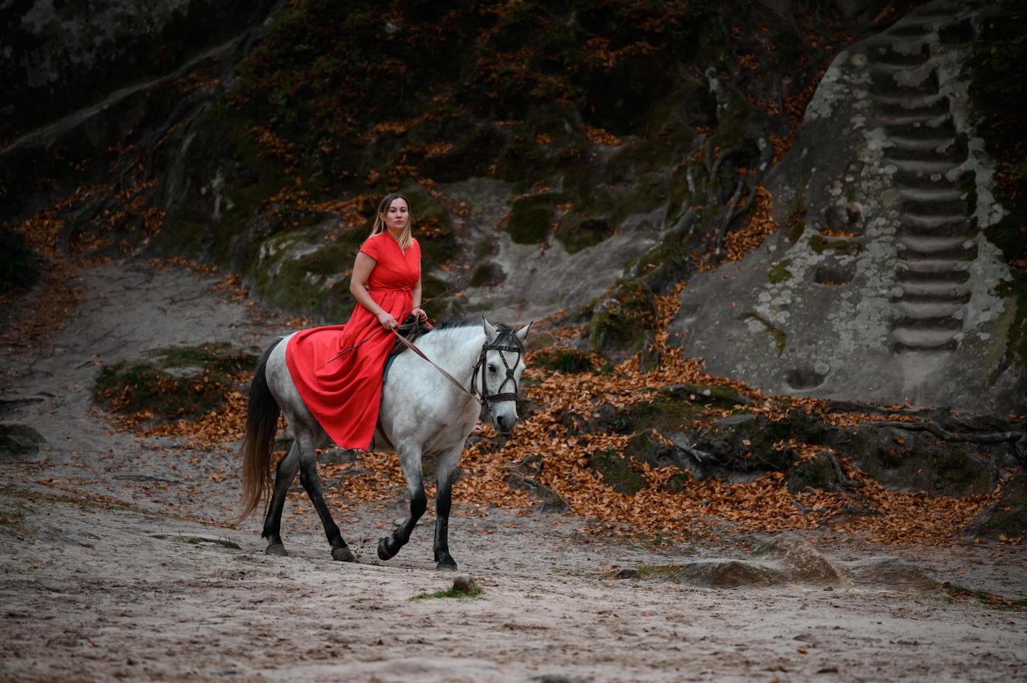 Dovbush rocks and horse riding, a woman riding a horse in a red dress with bare feet. photo