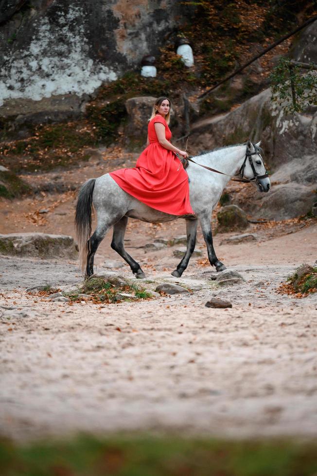 Dovbush rocks and horse riding, a woman riding a horse in a red dress with bare feet. photo