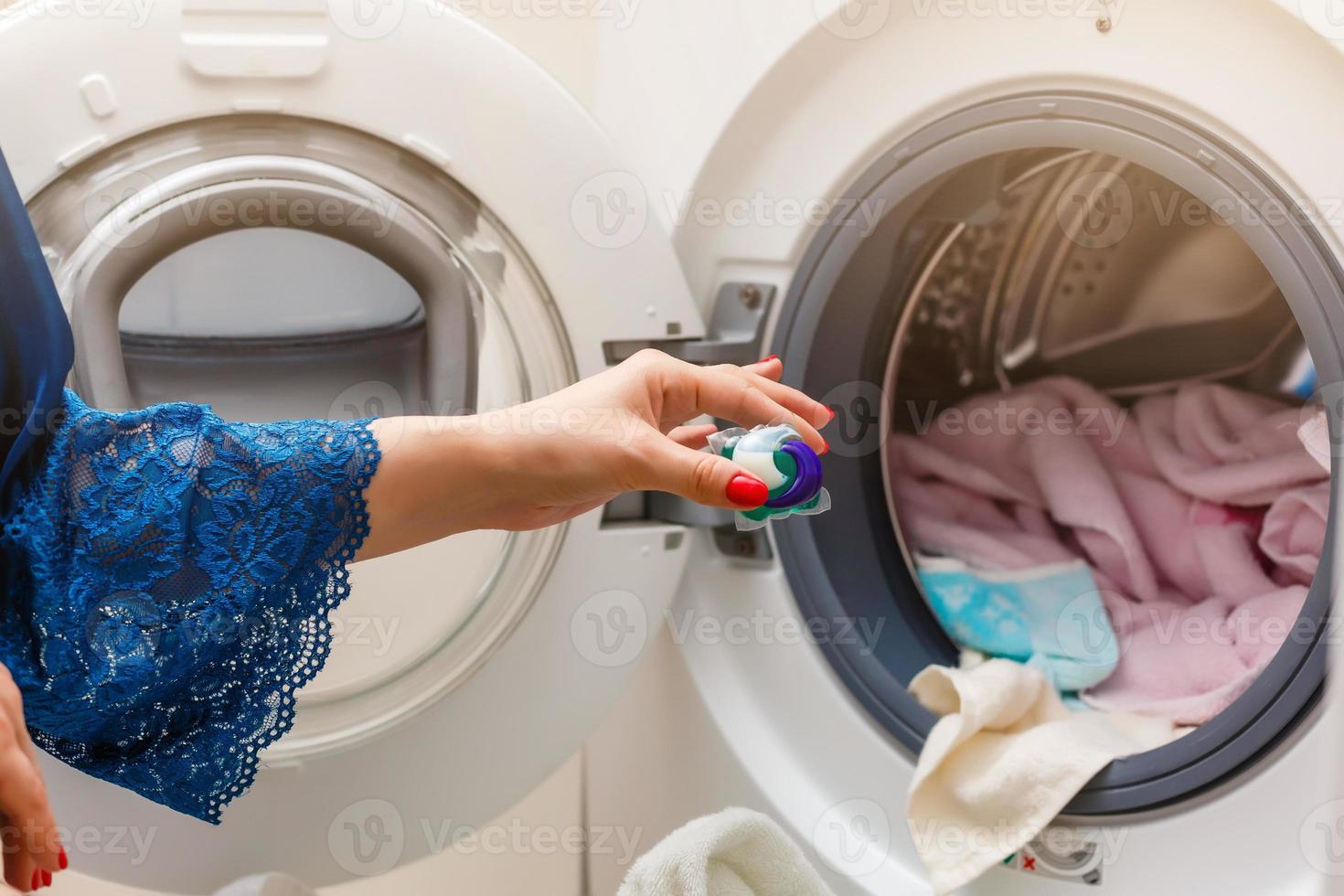 A close up of a young wife putting a cloth into washing machine photo