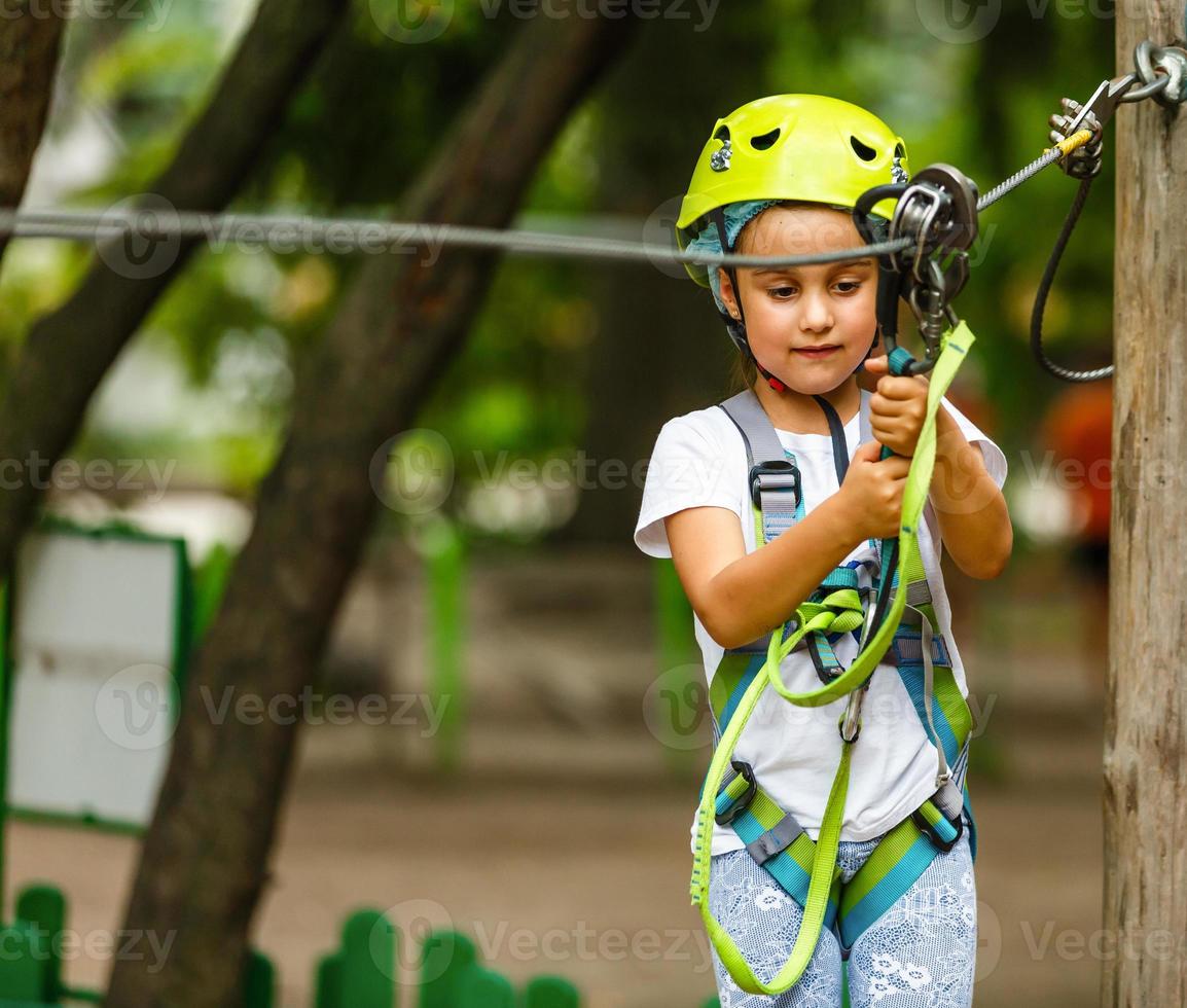 Adorable little girl enjoying her time in climbing adventure park on warm and sunny summer day photo