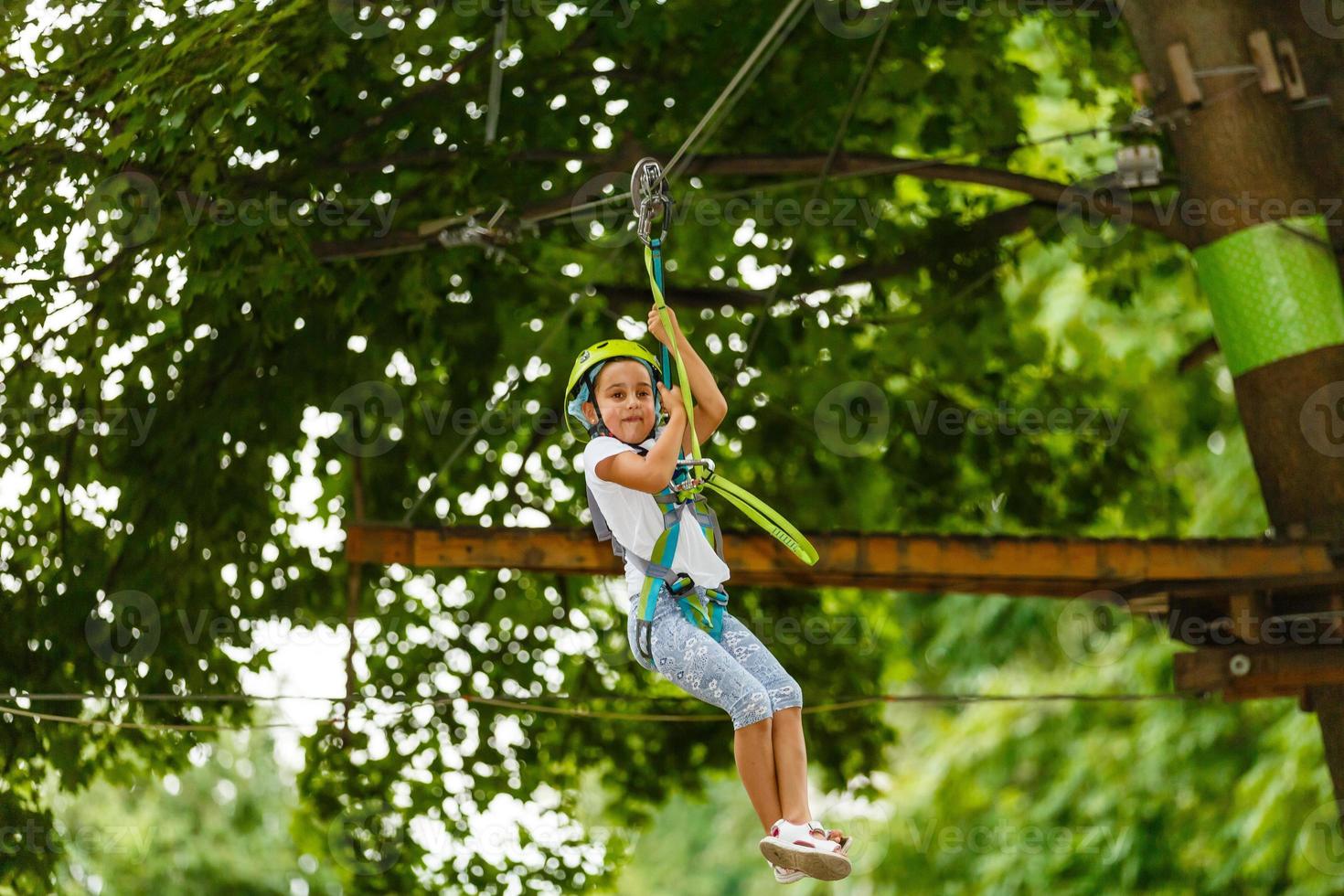 Portrait of little smiling girl in helmet and harness on trail in sky rope park in summer. photo