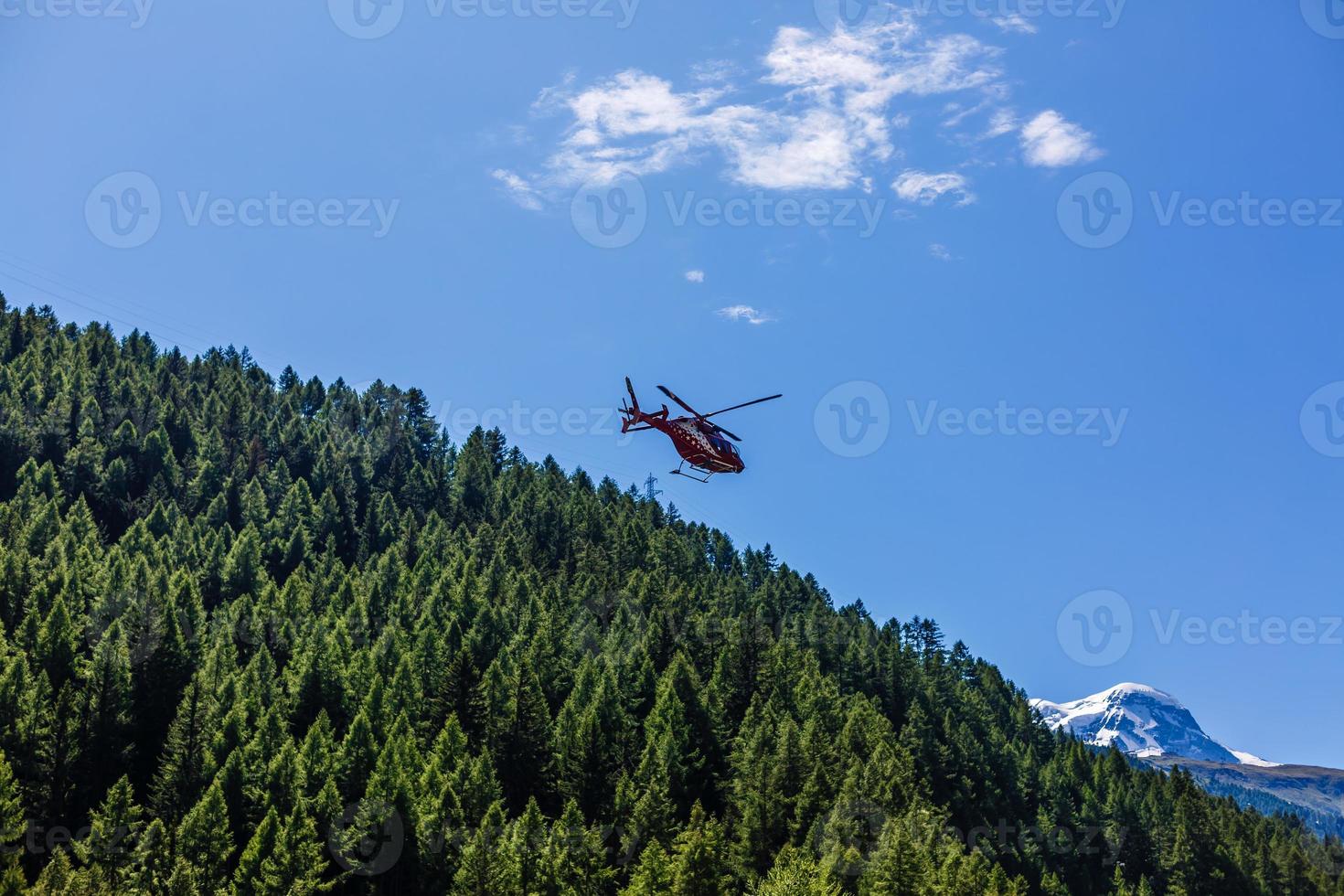red helicopter flying over the alps photo
