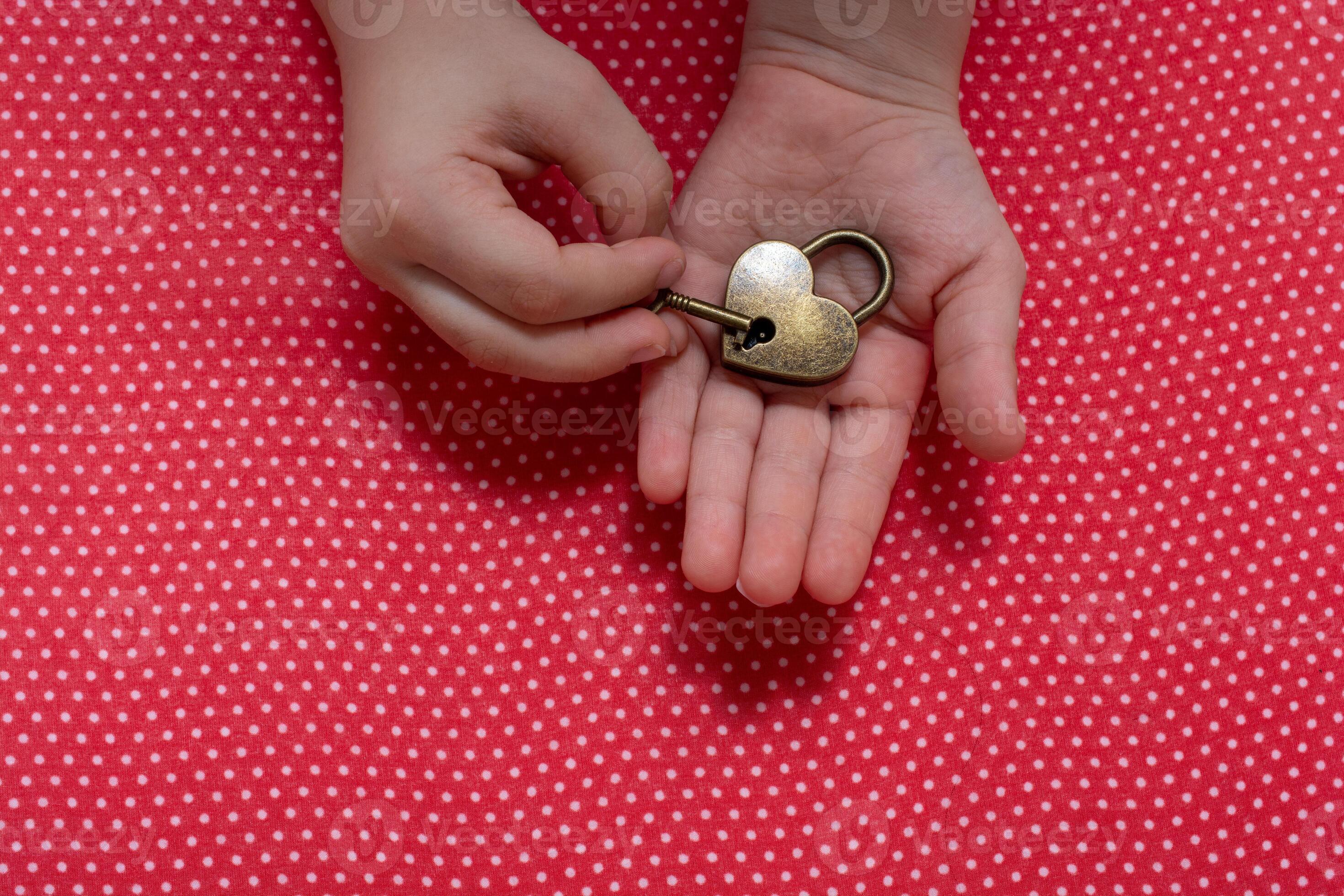 Hand holding a heart shaped lock and key on red background 16750909