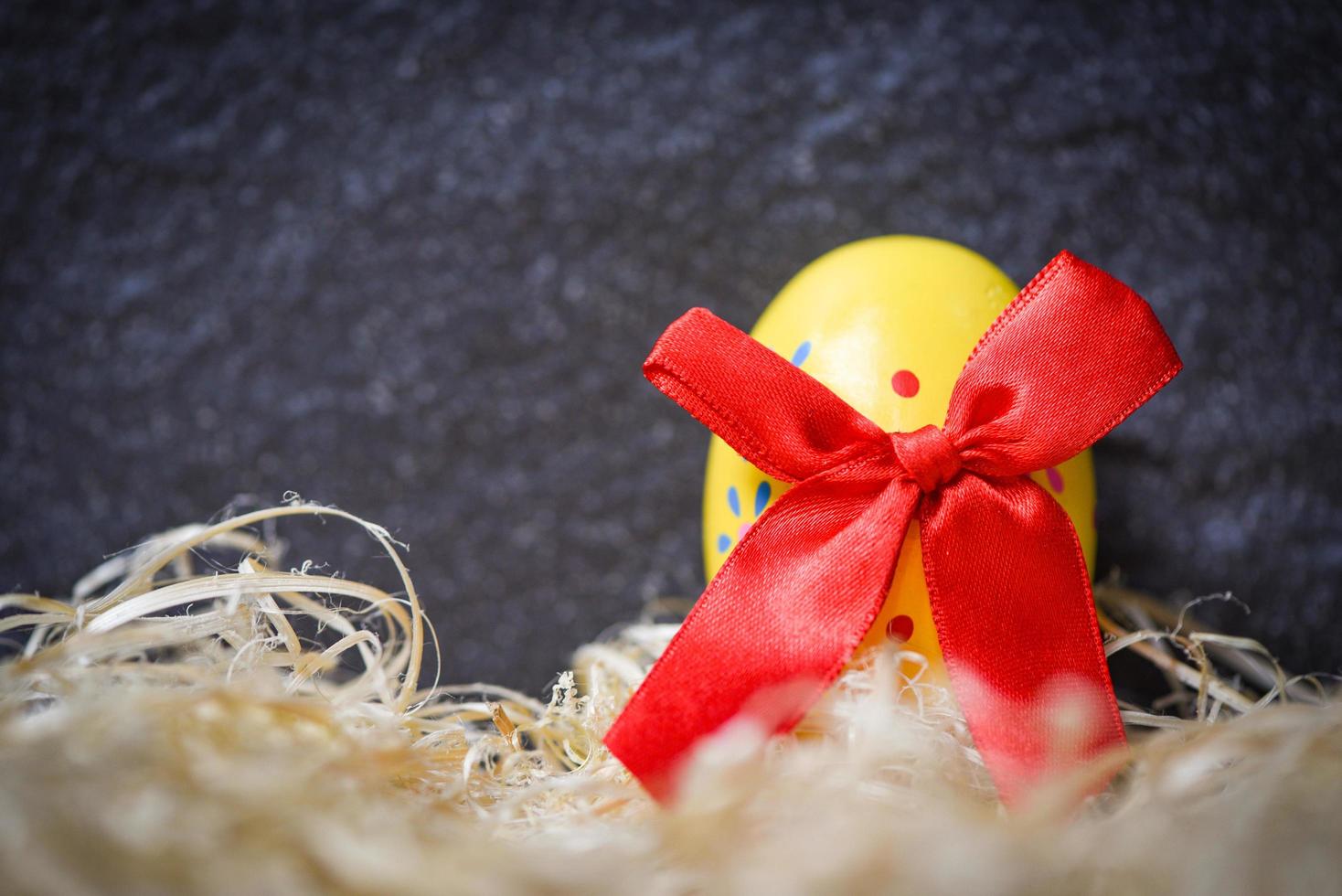 Yellow easter eggs with red ribbon bow in the nest on dark background photo