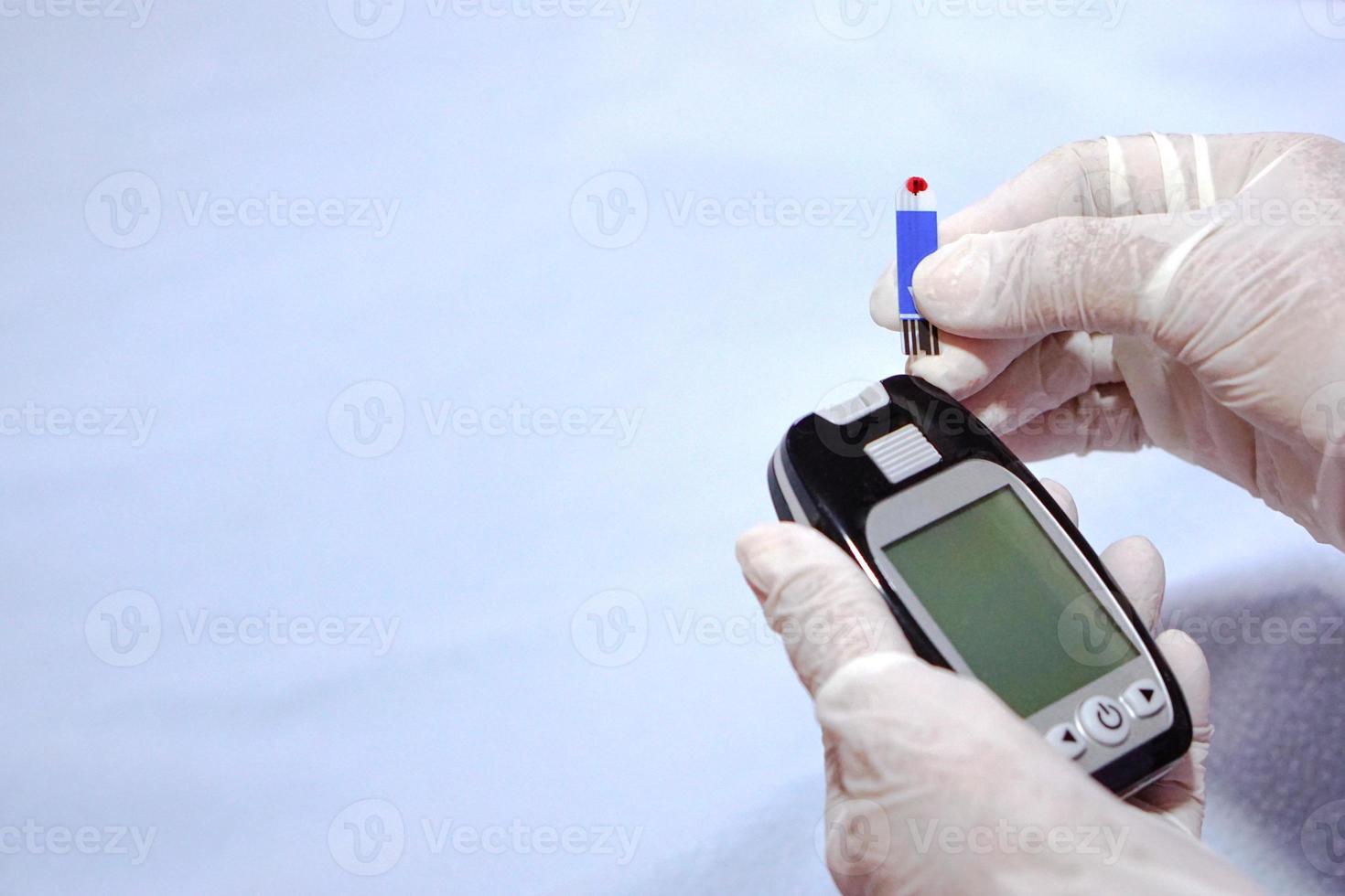 el médico usa guantes que sujetan el dispositivo para comprobar el nivel de azúcar en la sangre mediante glucosa y un lector de sangre. concepto de salud y examen físico. foto
