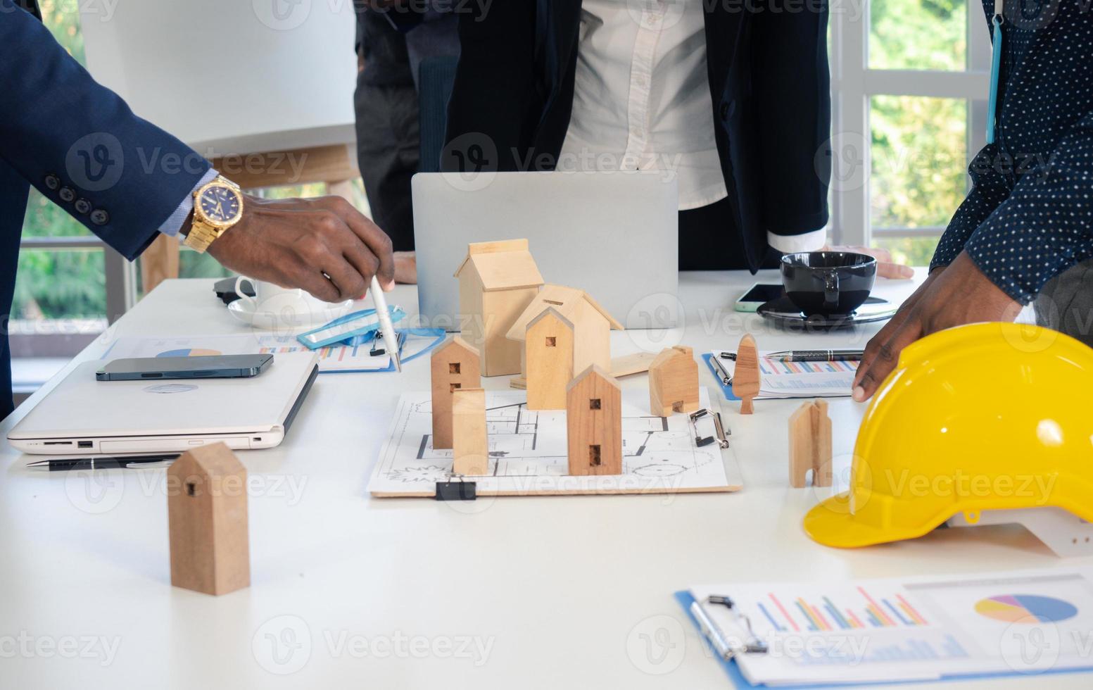 los colegas multirraciales de los empresarios intercambian ideas con modelos de casas y planos en la oficina. equipo de construcción profesional discutiendo la disposición de las líneas de servicio en el nuevo edificio. foto