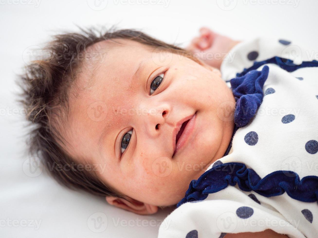 Portrait of three weeks Australian Asian newborn baby or infant lying on the white bed and opening her eyes. photo