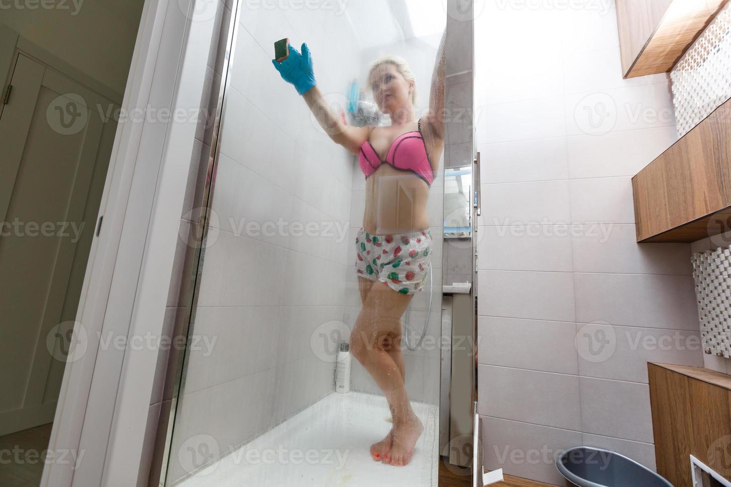 Mujer esbelta en traje de baño limpia baño y cabina de ducha. foto