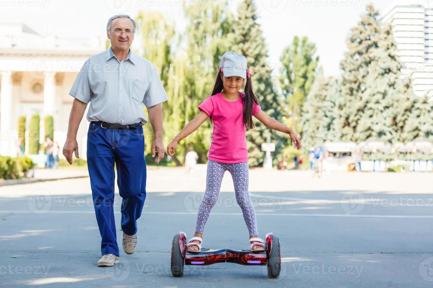 Little smiling girl learning to ride a hoverboard with her parents outdoors photo