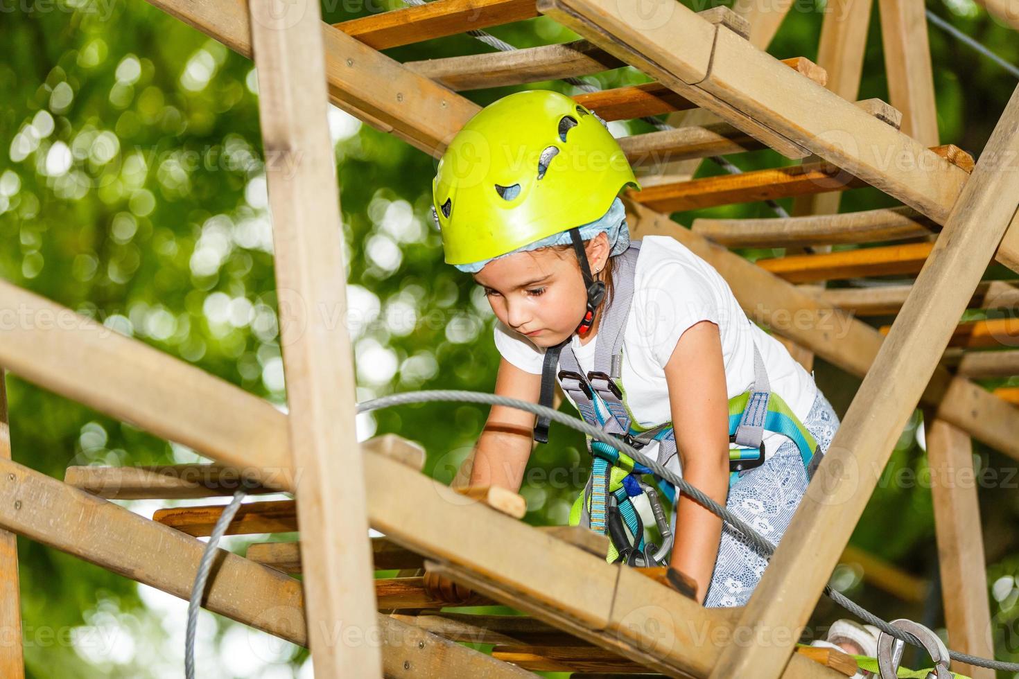 Adorable little girl enjoying her time in climbing adventure park on warm and sunny summer day. Summer activities for young kids. Child having fun on school vacations. photo