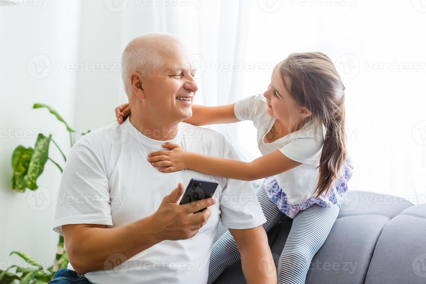 niña con su abuelo usando un teléfono inteligente en casa, espacio para texto. tiempo familiar foto