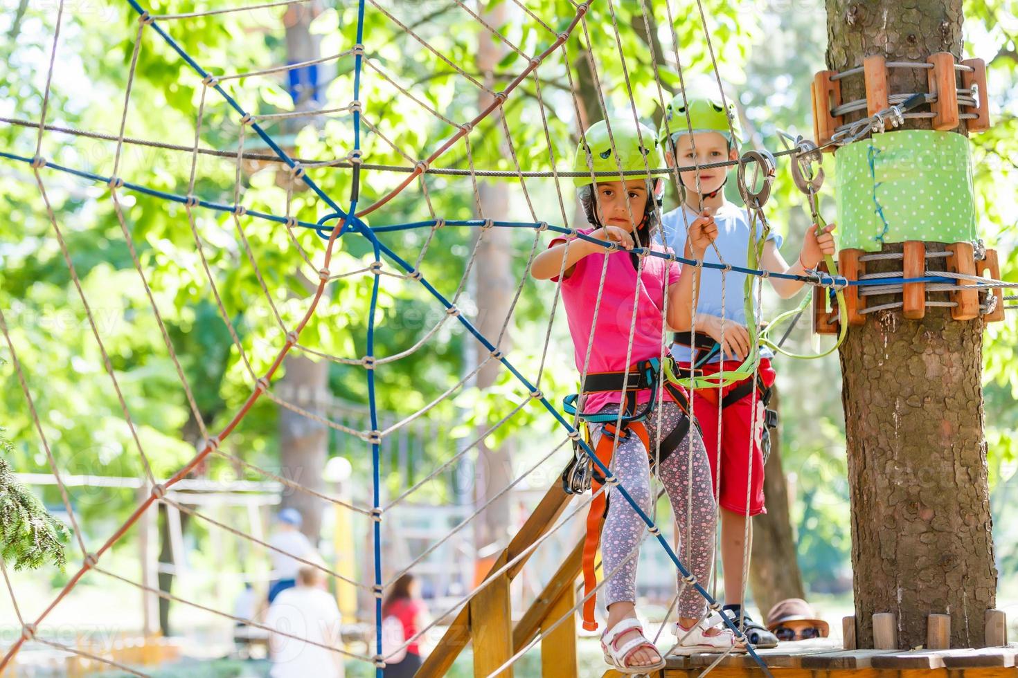 parque de cuerdas de escalada de aventura - niños en el parque de cuerdas del curso en casco de montaña y equipo de seguridad foto