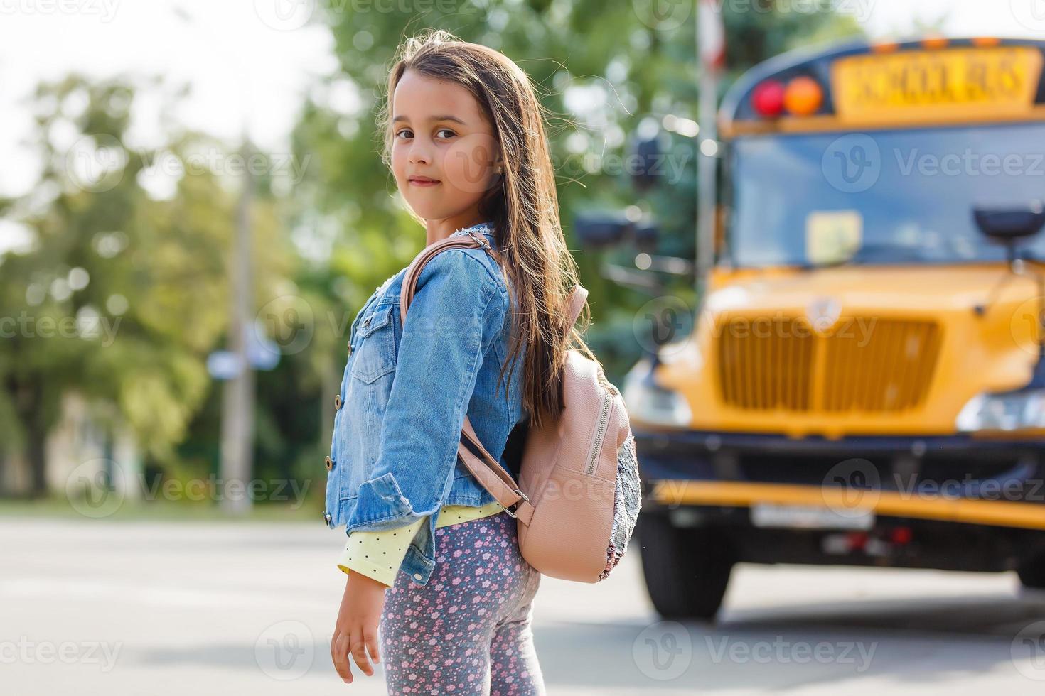 niña de pie junto a un gran autobús escolar con su mochila rosa. foto