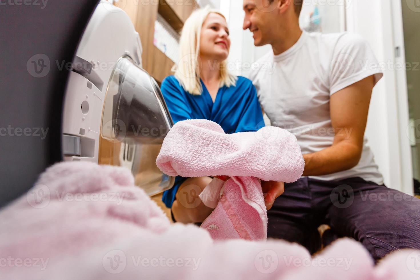 pareja divertida cargando ropa a la lavadora foto