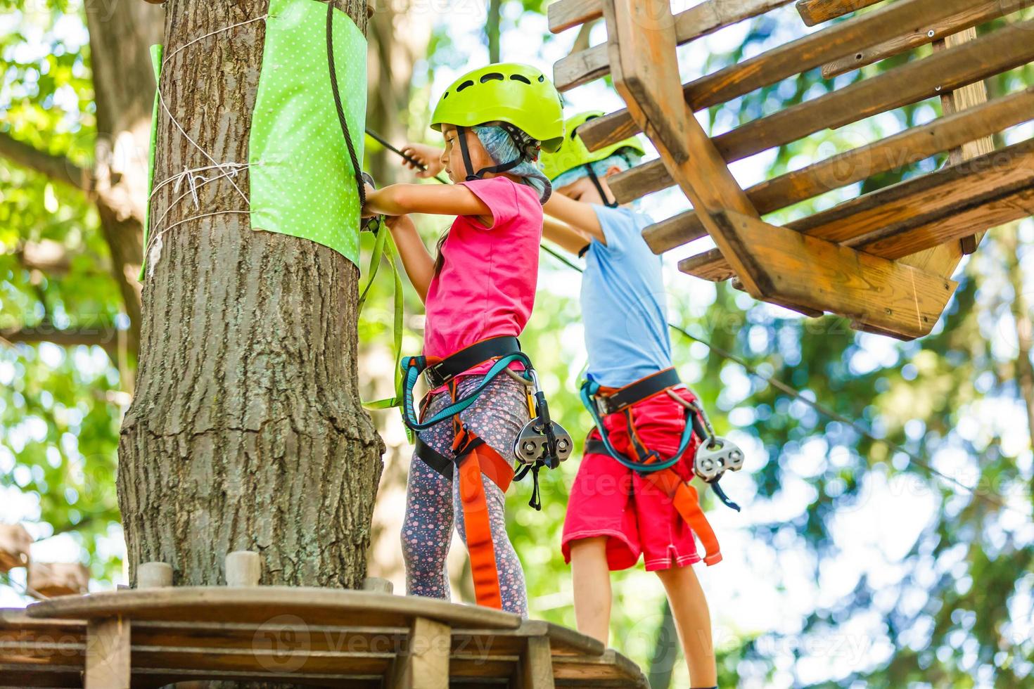 parque de cuerdas de escalada de aventura - niños en el parque de cuerdas del curso en casco de montaña y equipo de seguridad foto