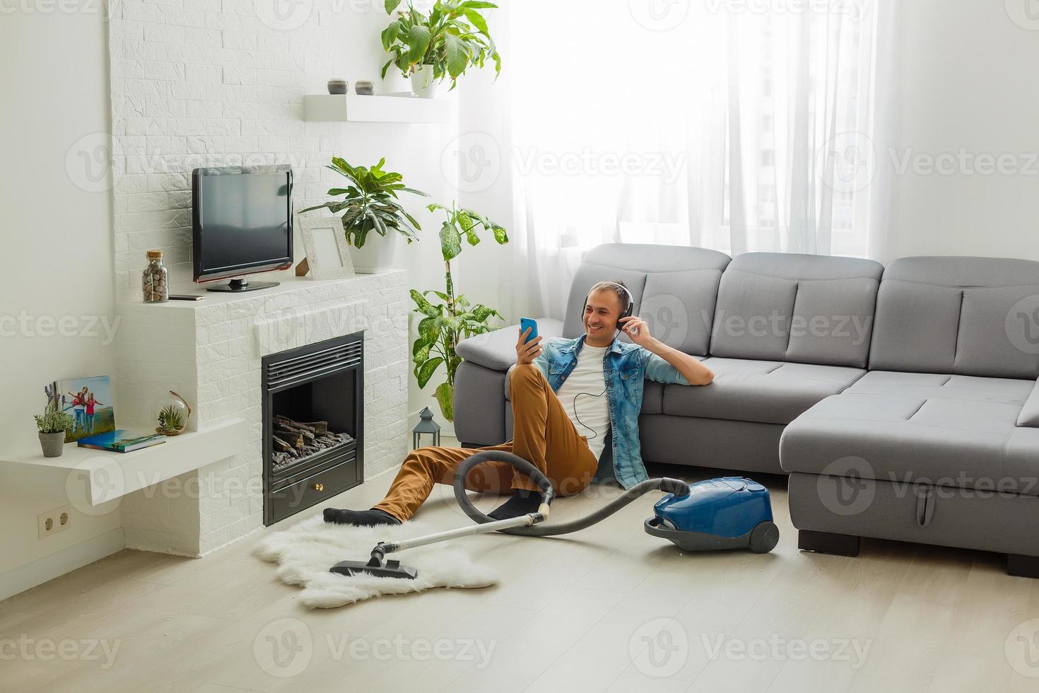 household and cleaning concept - indian man in headphones with vacuum cleaner at home photo