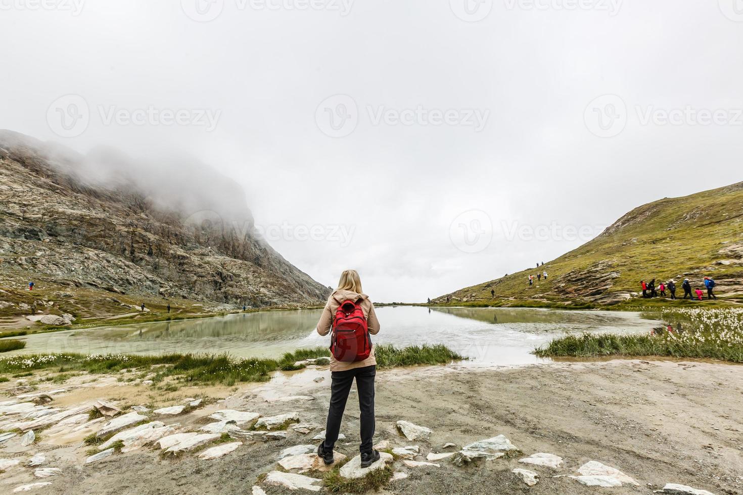 Young happy woman with backpack standing on a rock and looking to a valley below photo