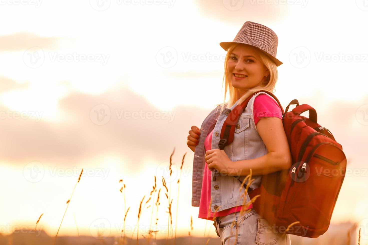 Hipster young girl with backpack enjoying sunset. Tourist traveler on background. photo