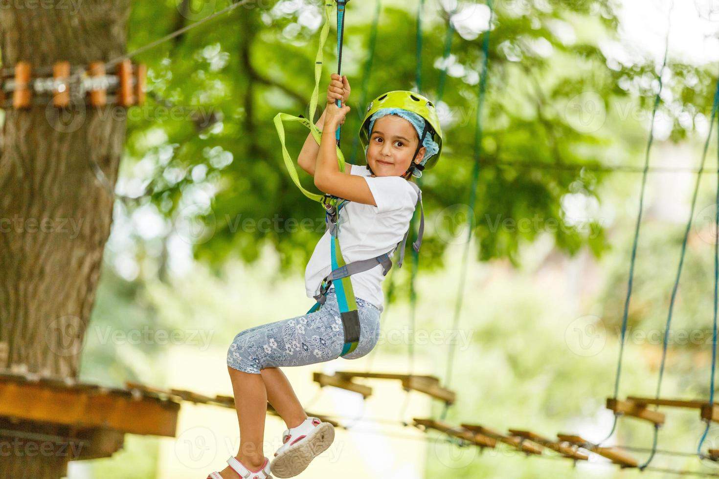 Adorable little girl enjoying her time in climbing adventure park on warm and sunny summer day. Summer activities for young kids. Child having fun on school vacations. photo