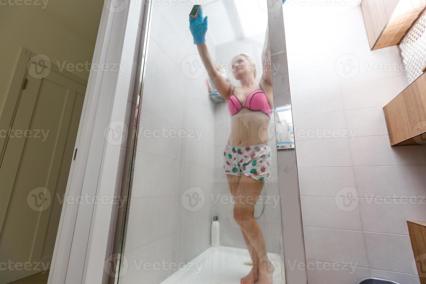 Mujer esbelta en traje de baño limpia baño y cabina de ducha. foto