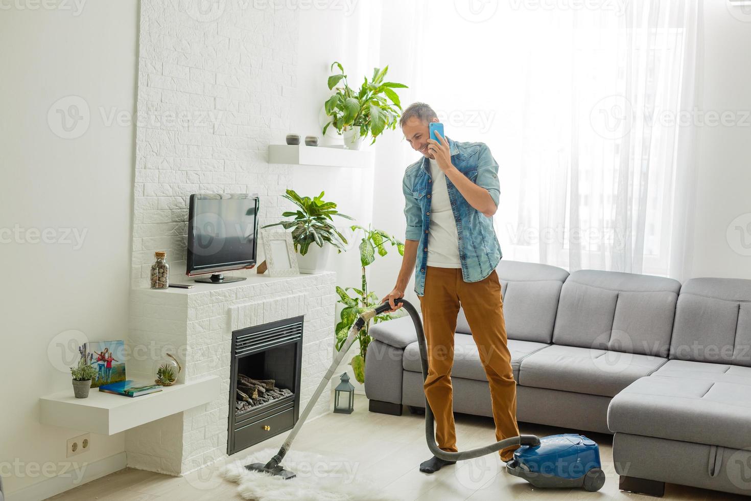 Caucasian handsome serious young man vacuuming cleaning modern apartment, clean up, housekeeper, guy doing domestic tasks and cleans living room using vacuum cleaner, householding photo