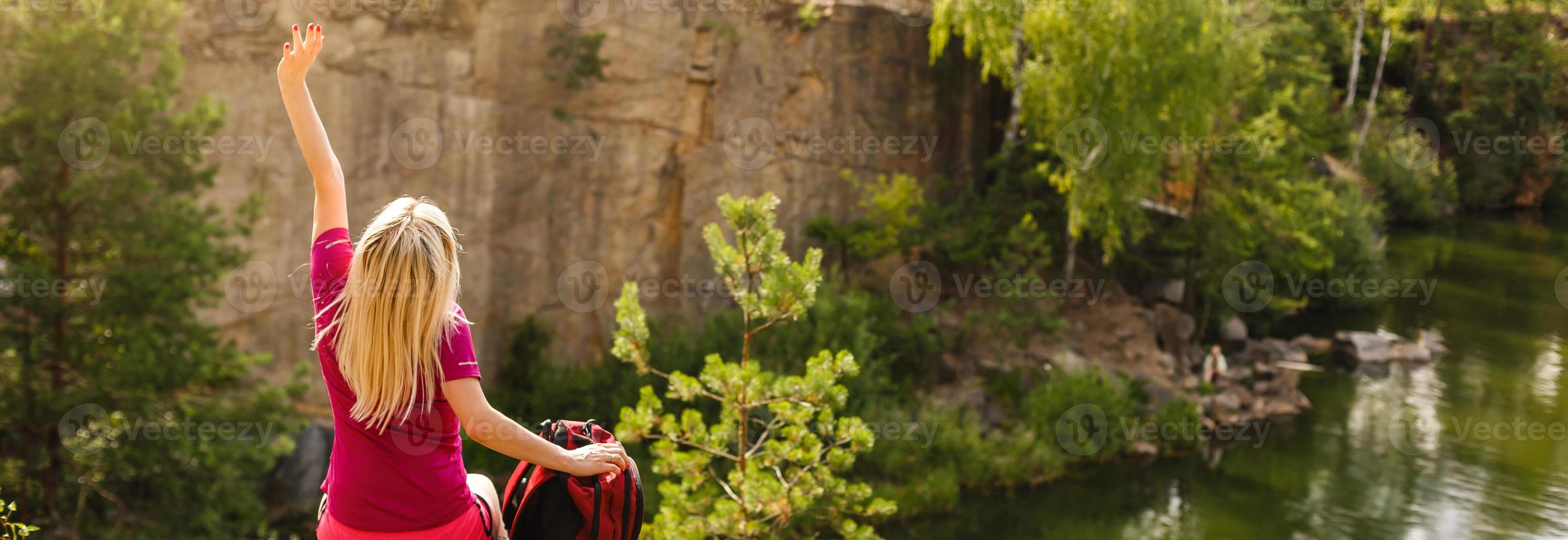 Rear view of woman hiker sitting on rock on top of hill while looking at sunset over photo