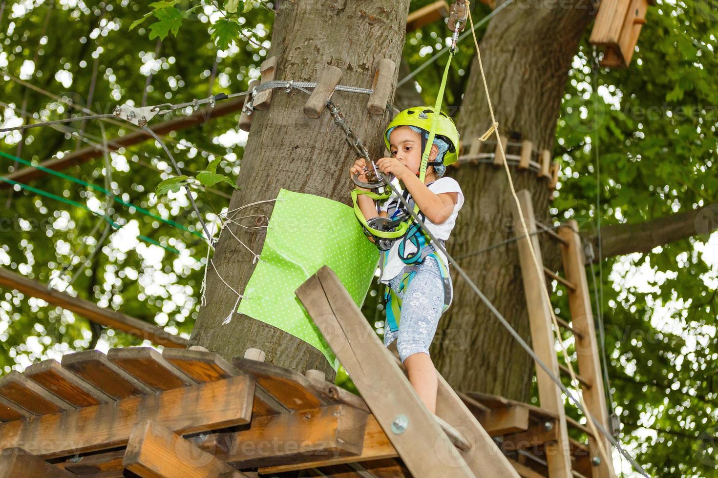 Adorable little girl enjoying her time in climbing adventure park on warm and sunny summer day. Summer activities for young kids. Child having fun on school vacations. photo