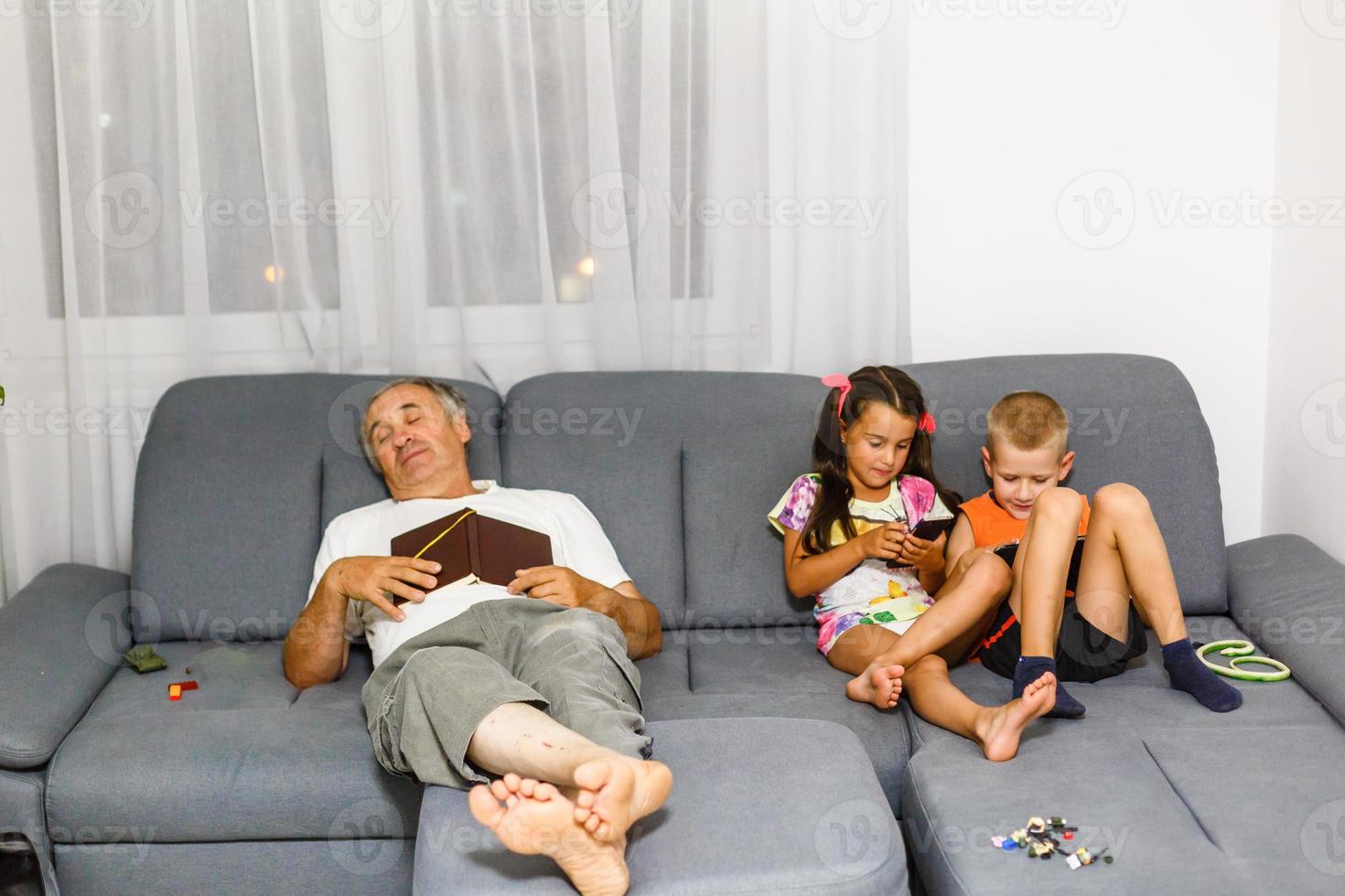 los niños juegan con su teléfono inteligente mientras el abuelo duerme foto