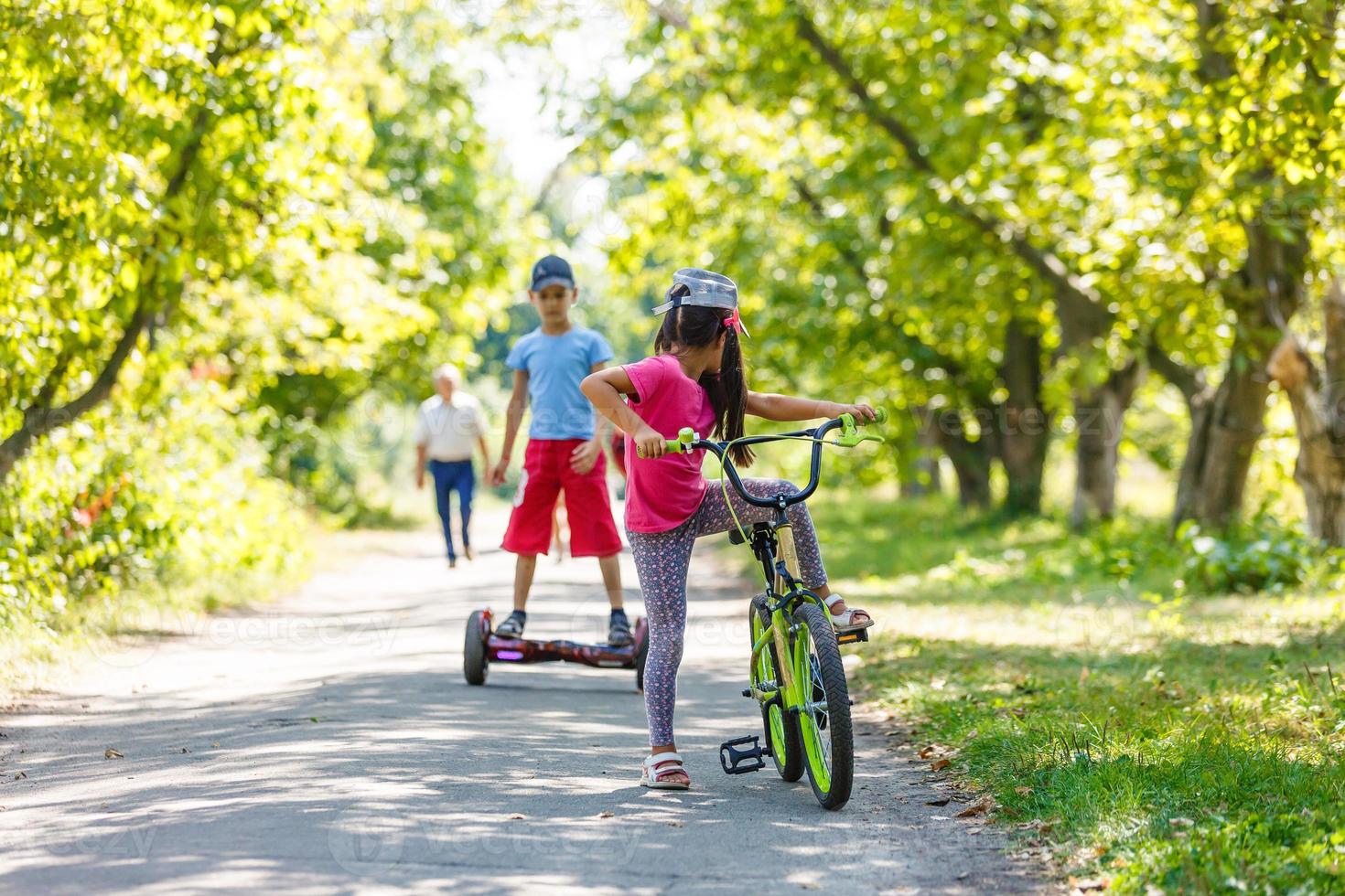 Girl on a bicycle and a boy on a gyroscope are riding together photo