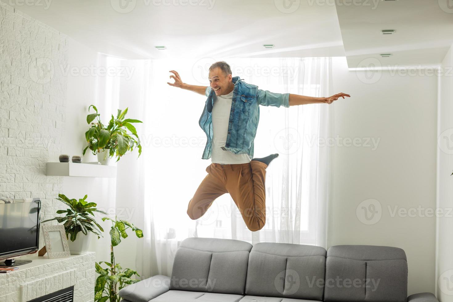 Caucasian man looks happy while dancing on the couch in the living room, the man jumps off the couch. Shot at home photo