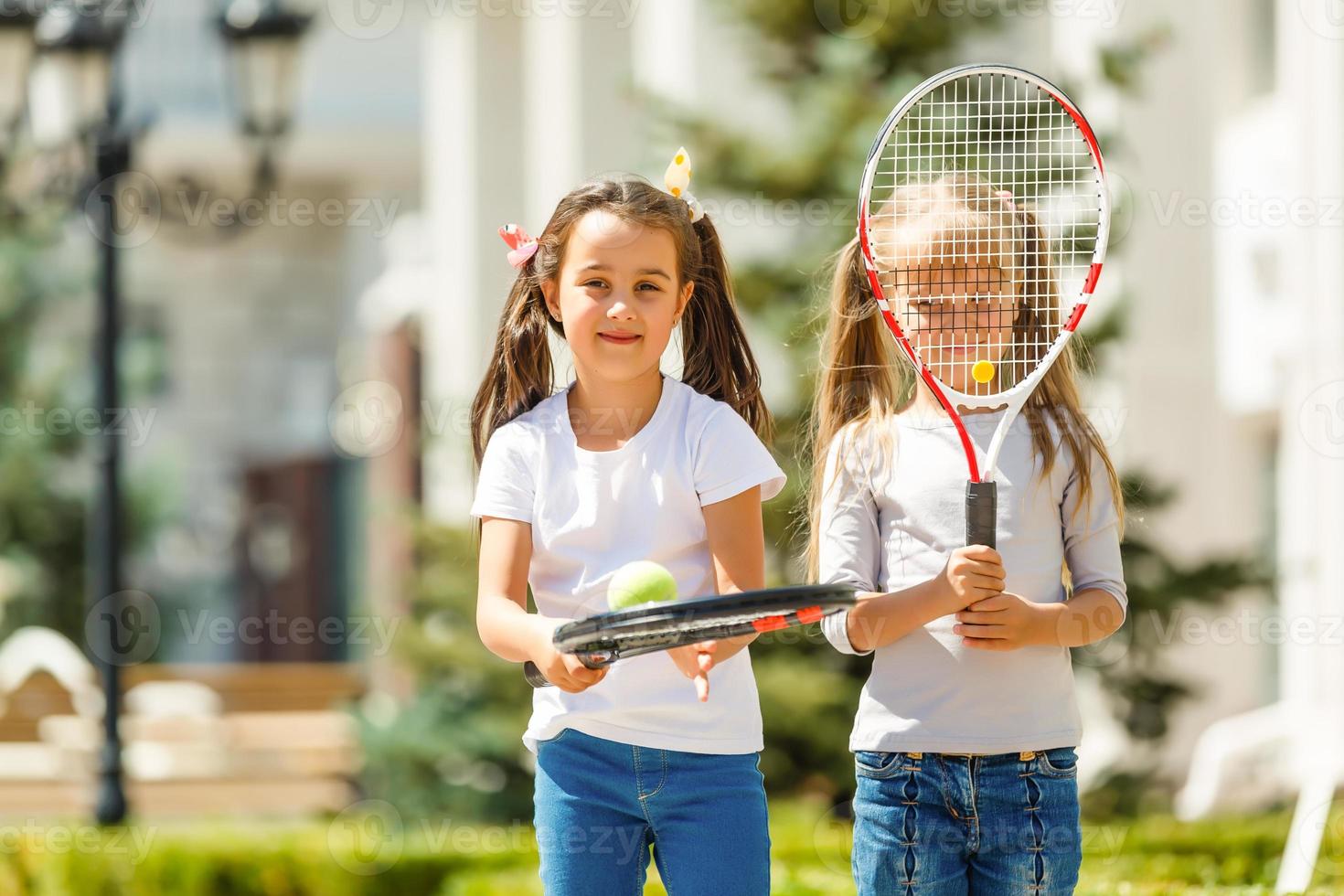 Happy preteen girls in sport outfits with tennis rackets on green grass background photo