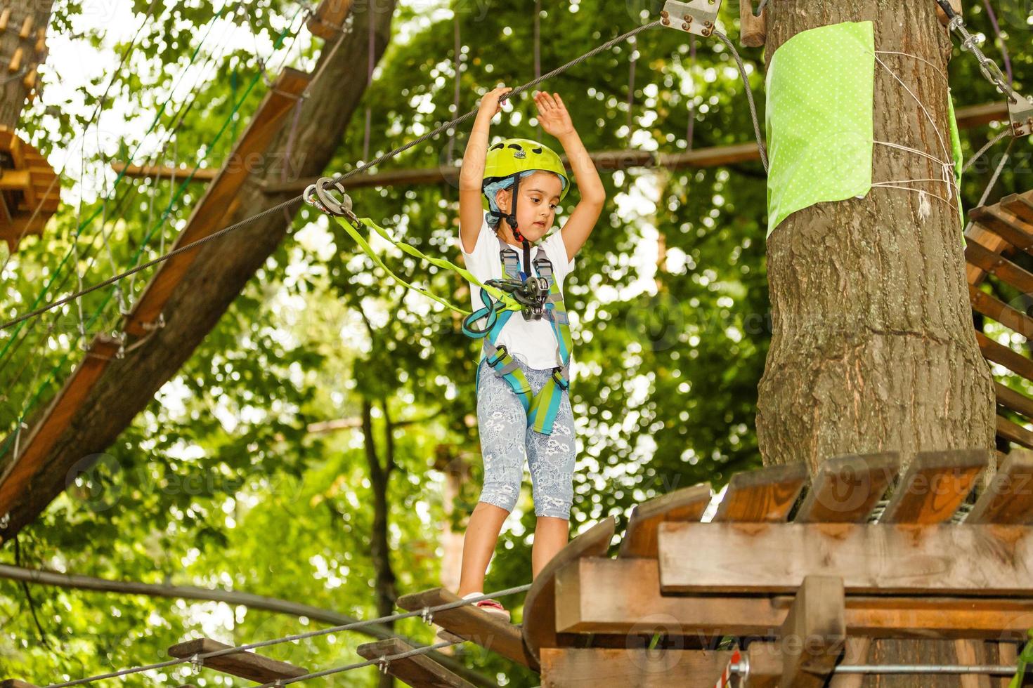 Little girl is standing on a rope, holding a rope with his hands. A child in a rope park passes obstacles photo