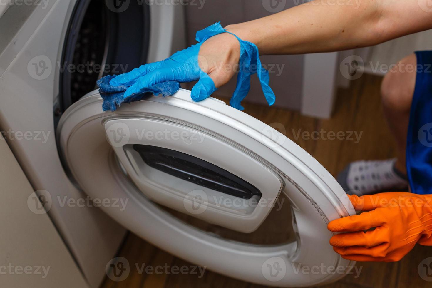 Hand in torn glove cleaning the washing machine. Regular clean up. Maid cleans house. photo