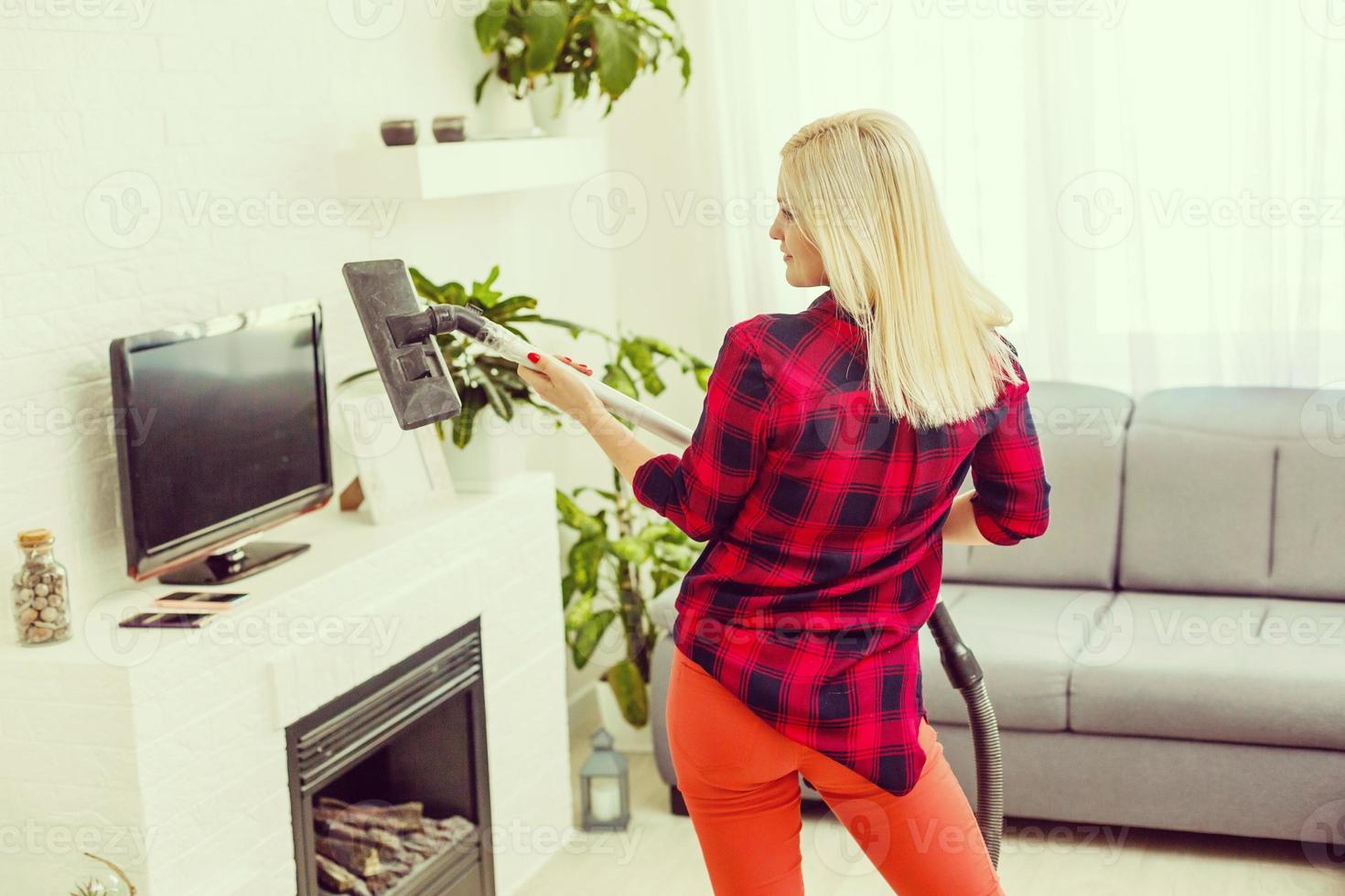 una joven y emocionada ama de casa sonriente se divierte mientras limpia el suelo con una aspiradora. mujer feliz haciendo tareas domésticas en casa disfruta de la música con auriculares. foto