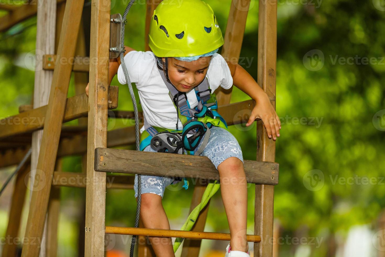 Adorable little girl enjoying her time in climbing adventure park on warm and sunny summer day. Summer activities for young kids. Child having fun on school vacations. photo