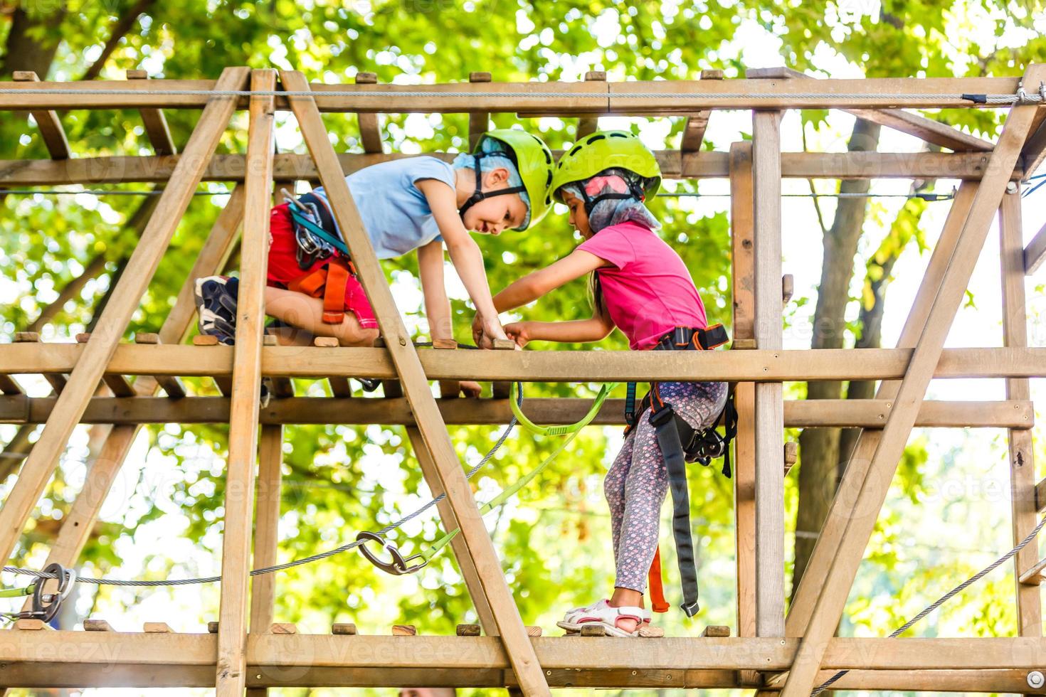 parque de cuerdas de escalada de aventura - niños en el parque de cuerdas del curso en casco de montaña y equipo de seguridad foto