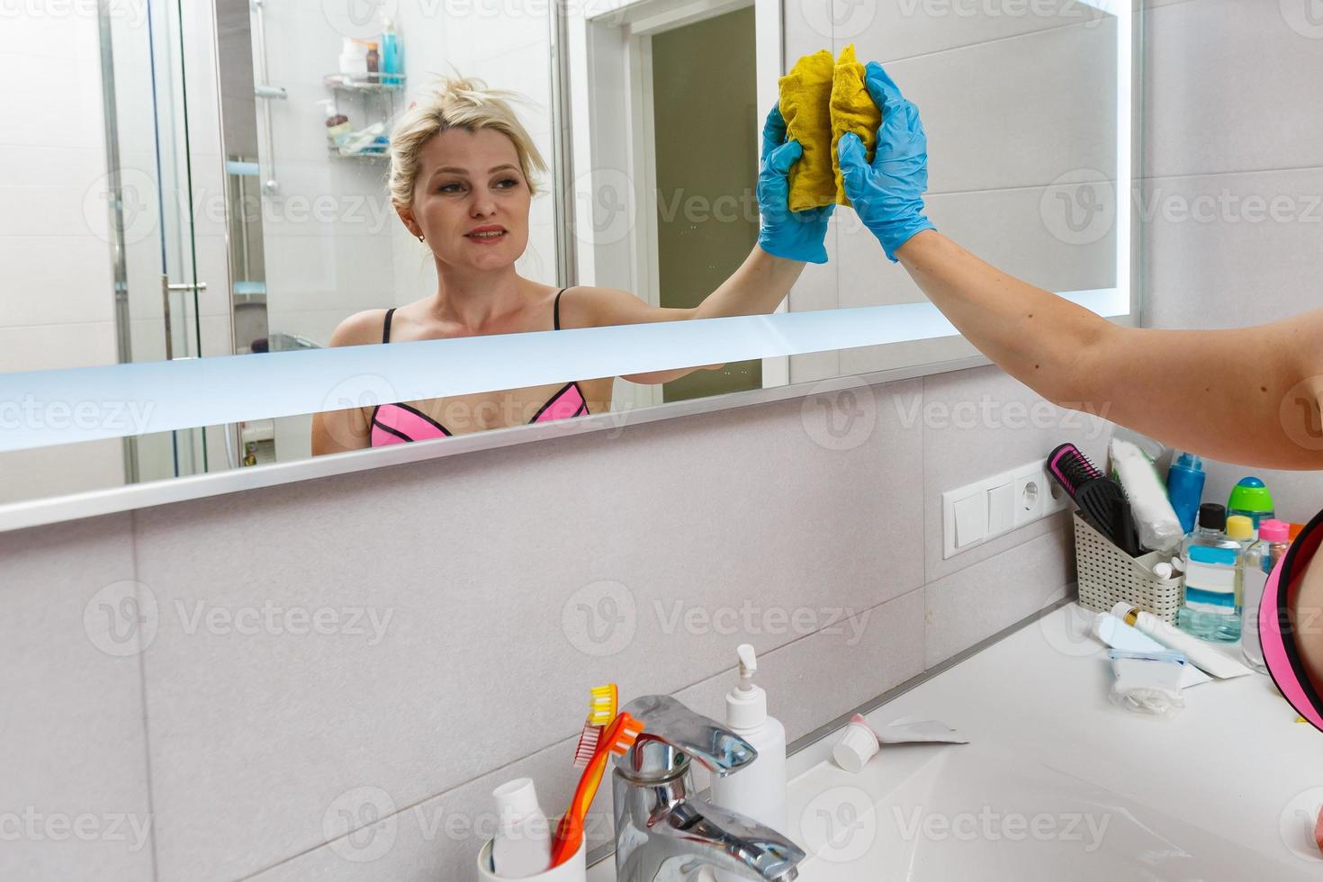 Slender woman in swimsuit cleans bathroom and shower cabin photo