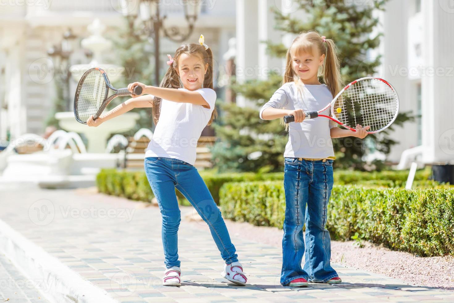 Happy preteen girls in sport outfits with tennis rackets on green grass background photo