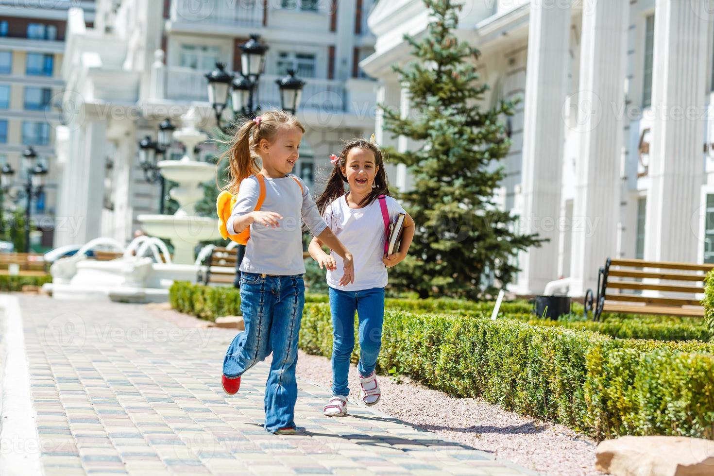 two school girls wearing backpack outside the primary school. schoolgirl, elementary school student going from school, graduation, summer holidays. photo