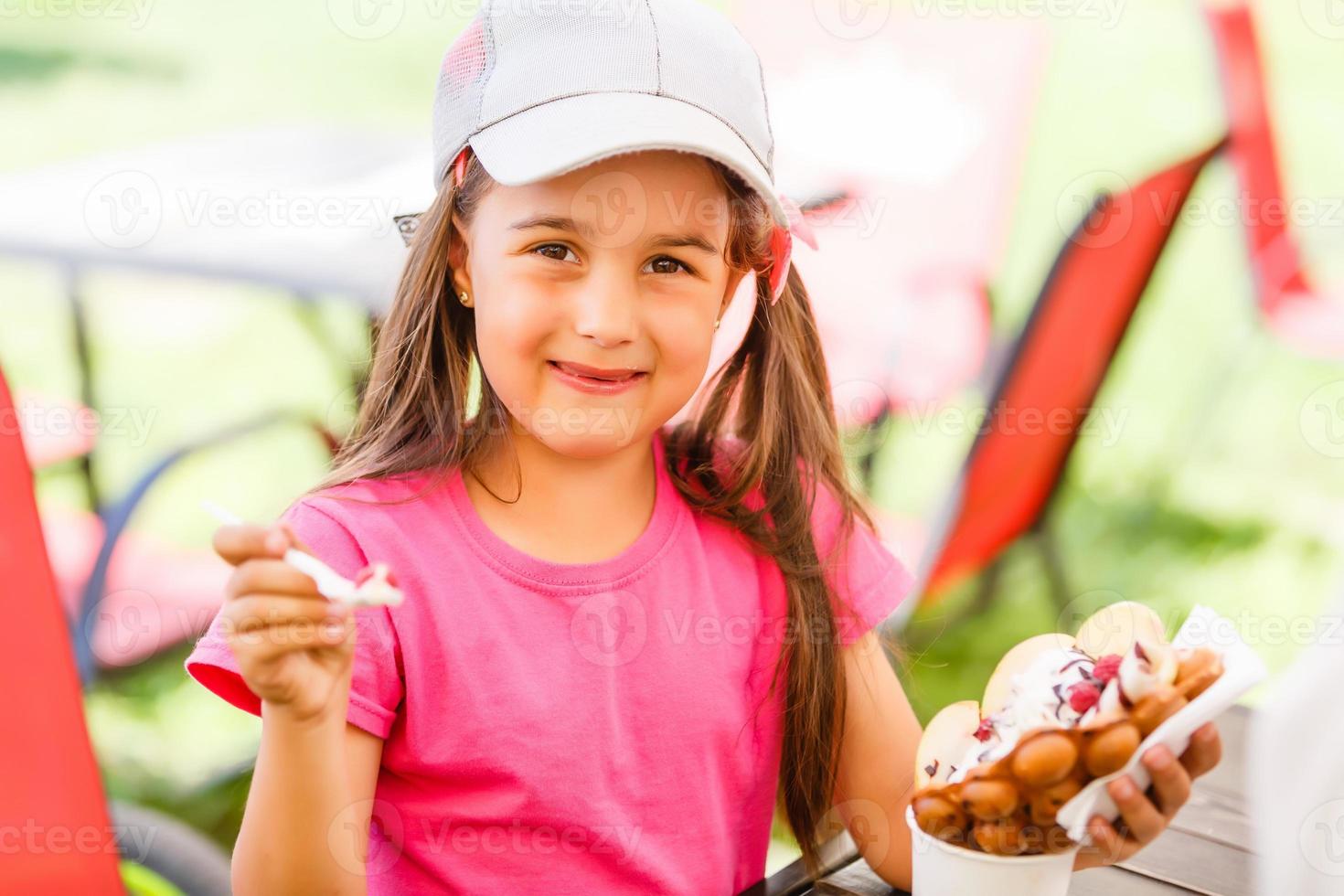Beautiful little girl eating a bubble waffle with ice cream in the summer photo