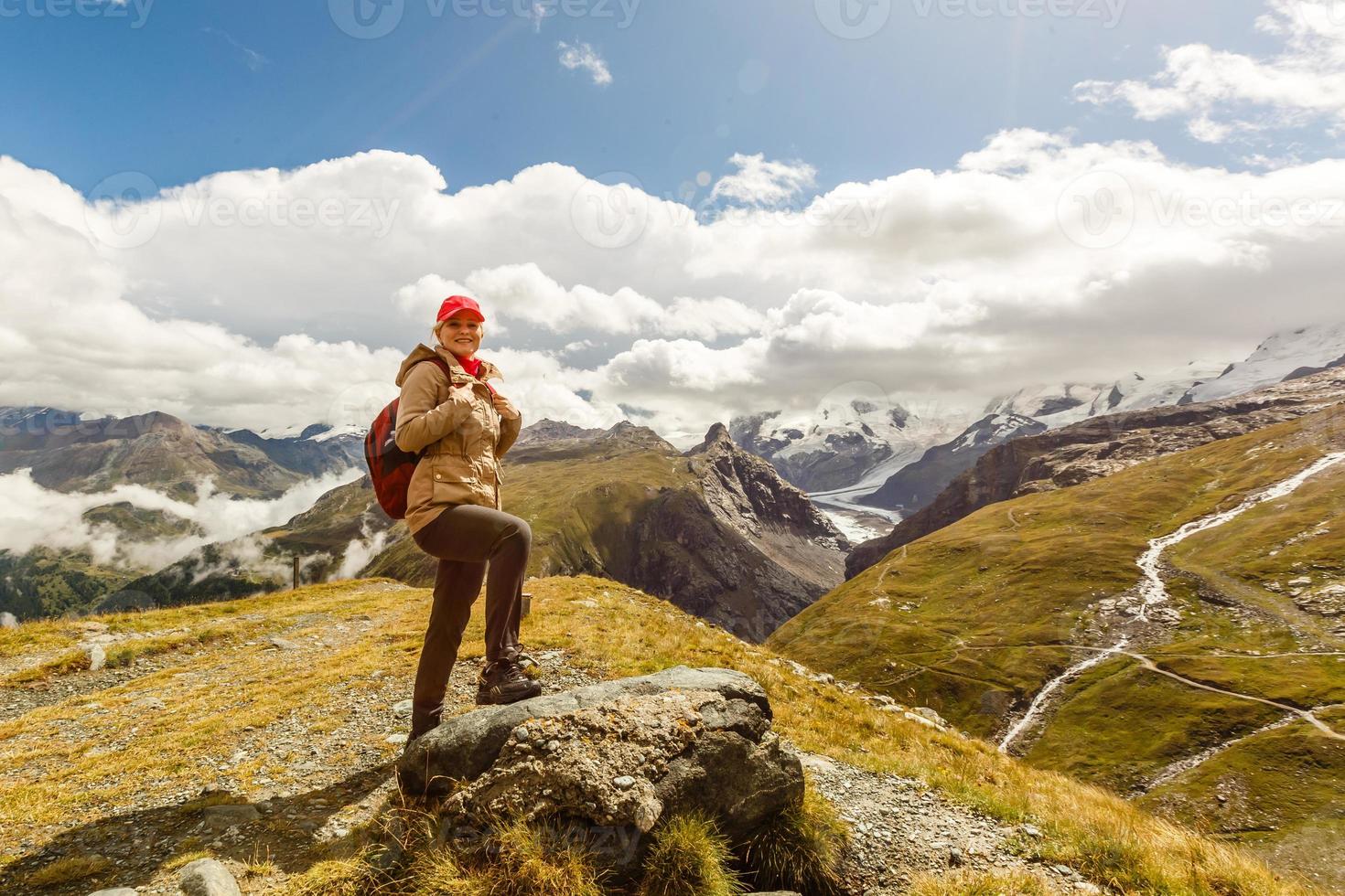 Young happy woman with backpack standing on a rock and looking to a valley below photo