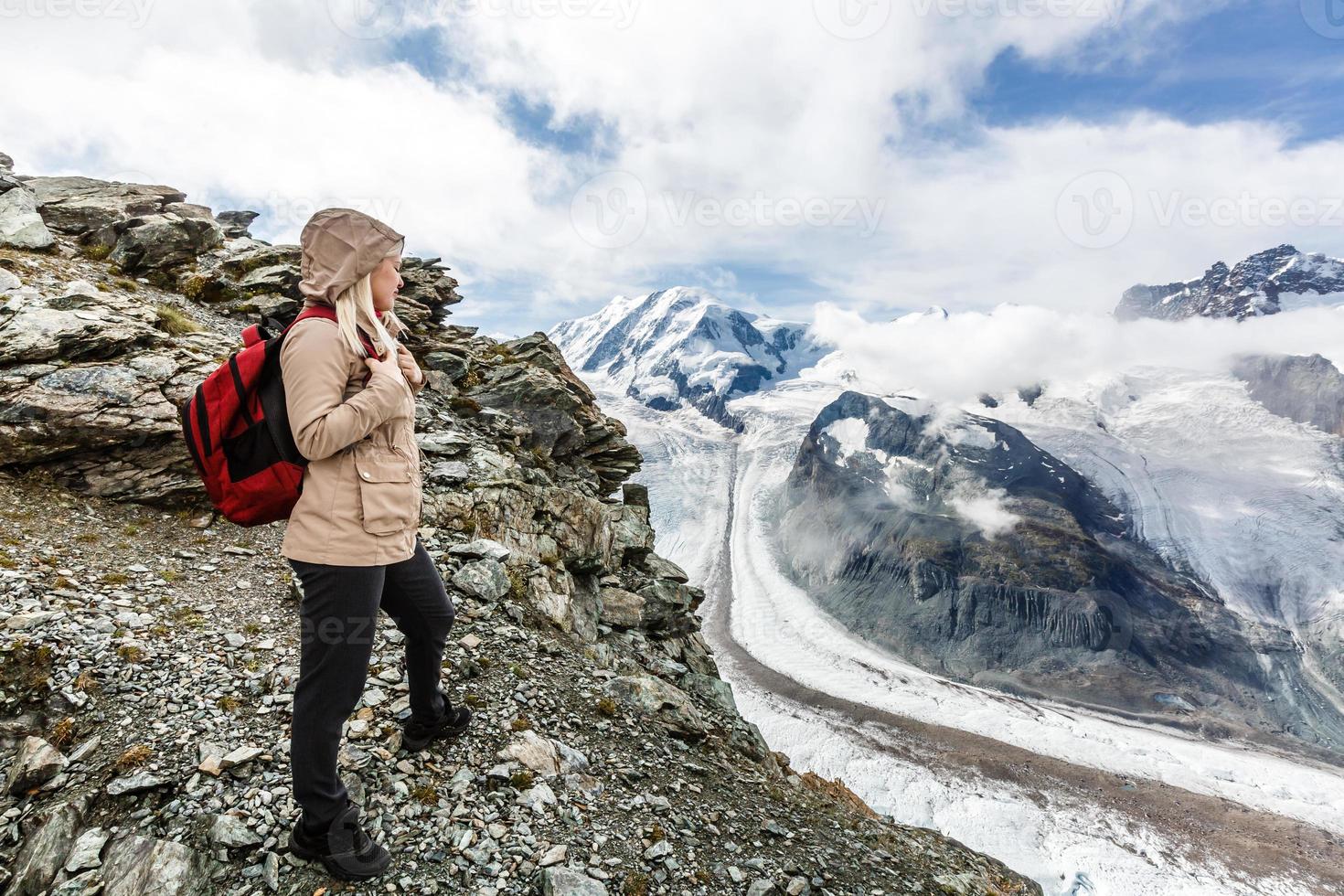 Young happy woman with backpack standing on a rock and looking to a valley below photo