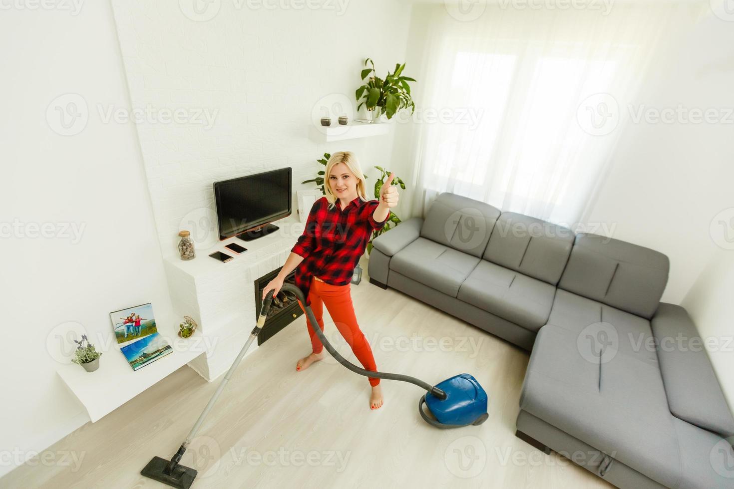 Young smiling woman vacuum cleaning the carpet in the living room, modern scandinavian interior. Busy, cleaning day. Home, housekeeping concept photo