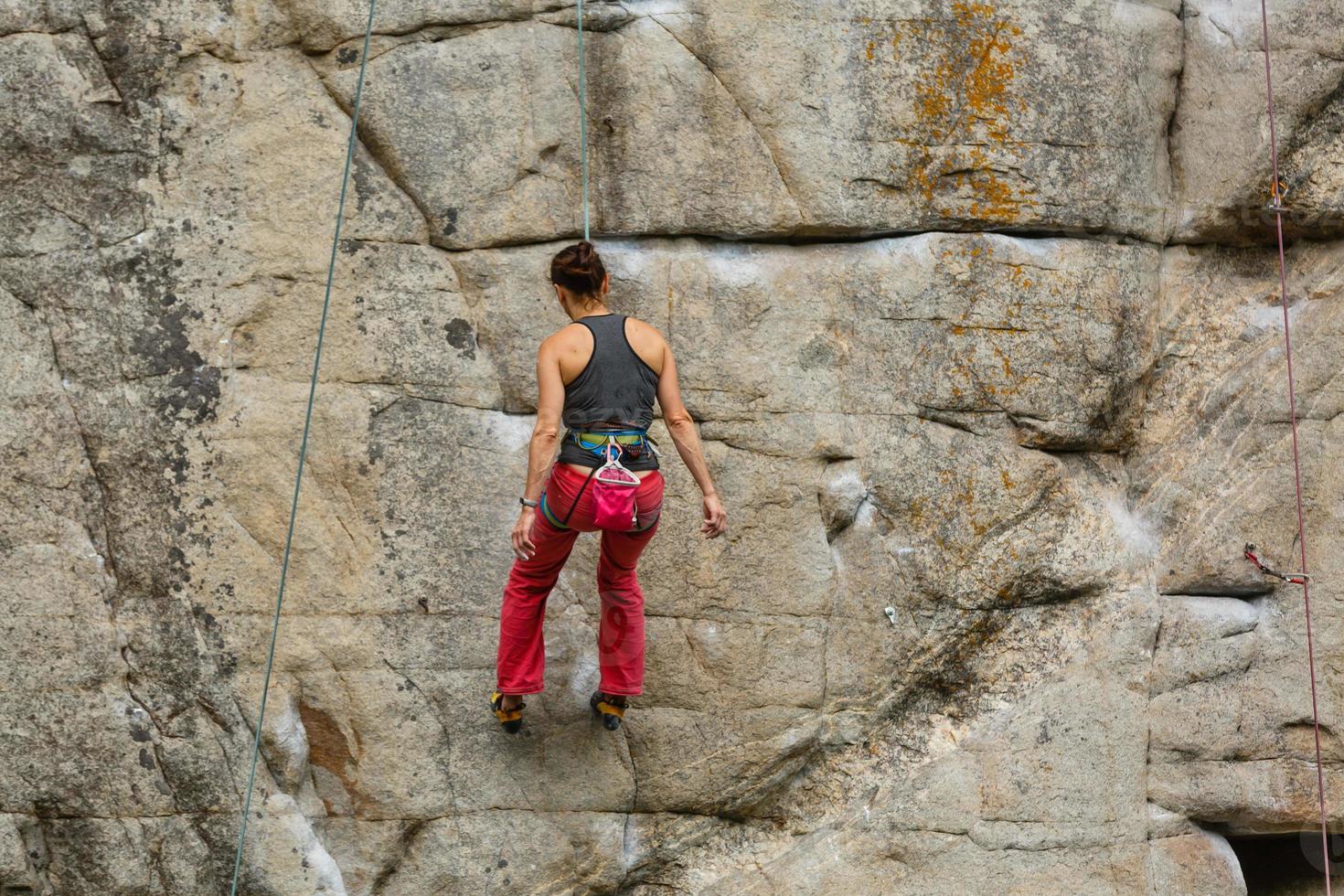 A young woman with a rope engaged in the sports of rock climbing on the rock. photo