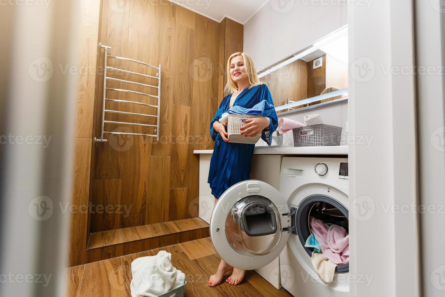 Beautiful young woman is smiling while doing laundry at home. photo