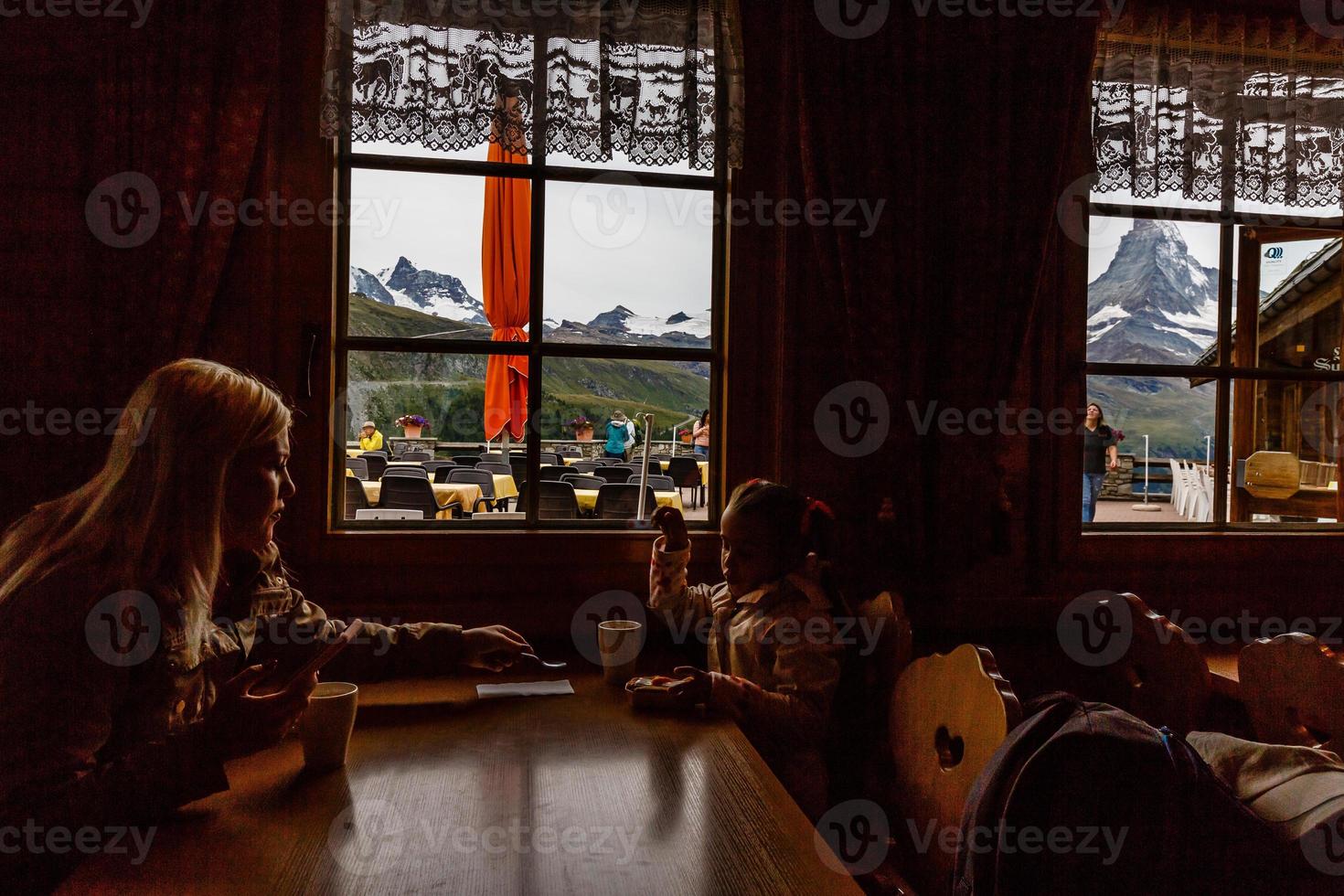 Mom with daughter drinking warm tea in the rustic wooden cafe on mountain, alpine view, snow on hills. Winter weekend. photo