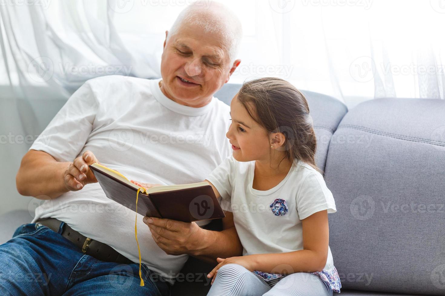 Happy little girl with grandfather reading story book at home photo