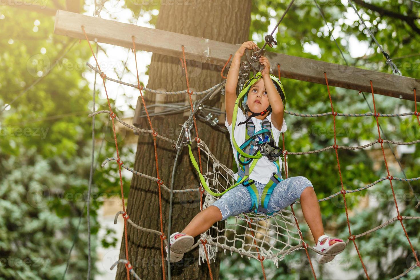 Adorable little girl enjoying her time in climbing adventure park on warm and sunny summer day. Summer activities for young kids. Child having fun on school vacations. photo