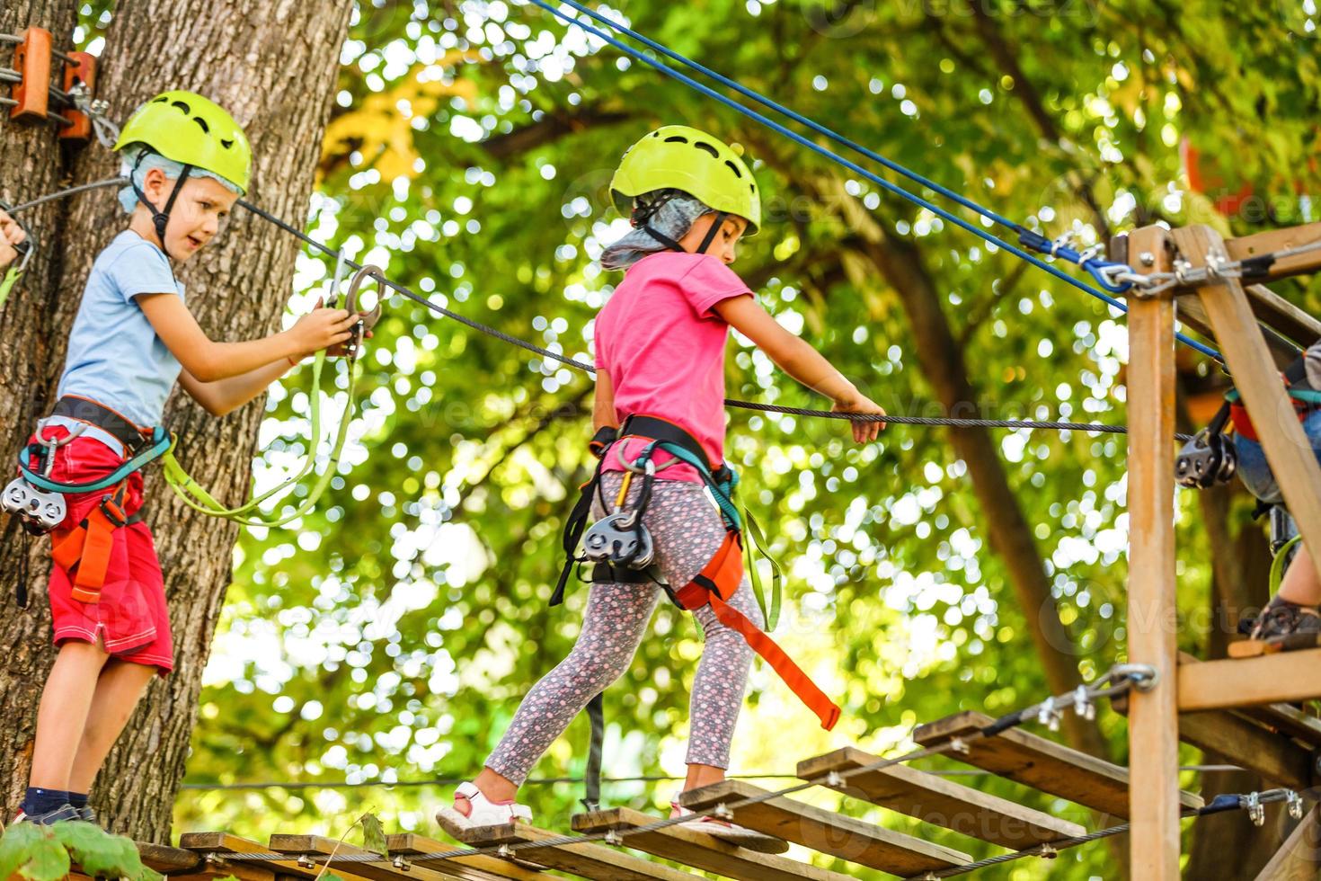 parque de cuerdas de escalada de aventura - niños en el parque de cuerdas del curso en casco de montaña y equipo de seguridad foto