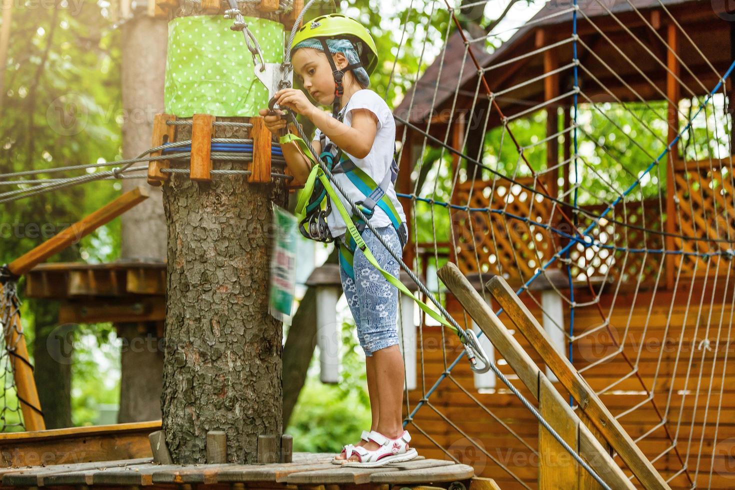 Happy school girl enjoying activity in a climbing adventure park on a summer day photo